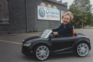 Kid in toy car in front of O'Hara Automotive